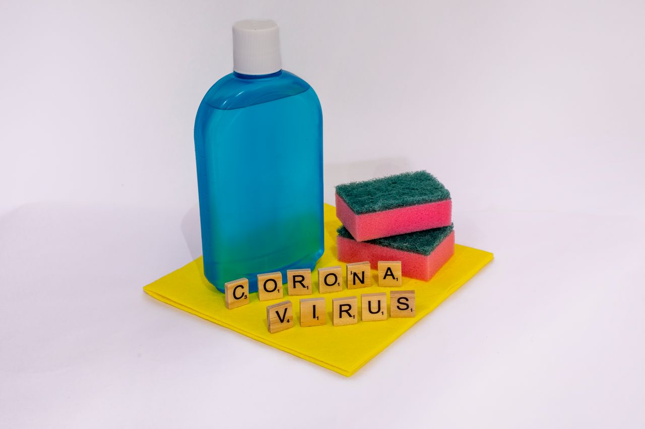 Cleaning products with scrabble tiles spelling coronavirus on a white surface.
